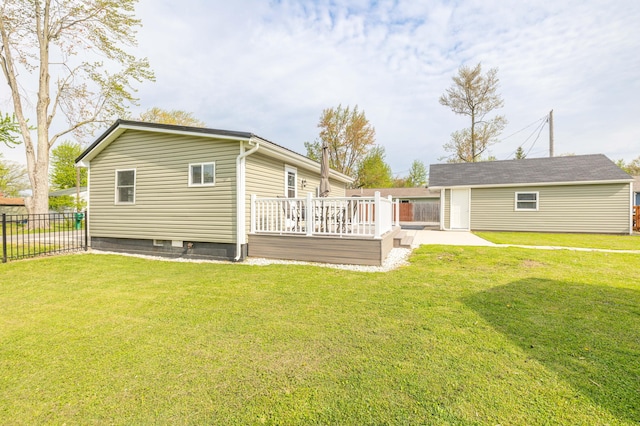 back of property with a lawn, fence, an outbuilding, and a deck