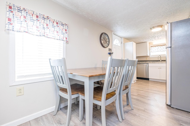 dining space featuring light wood-type flooring, a textured ceiling, and baseboards