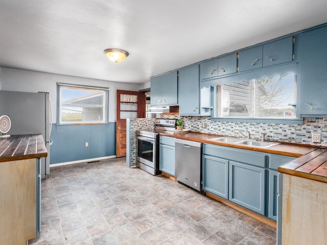 kitchen featuring stainless steel appliances, a sink, backsplash, and blue cabinetry