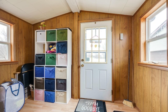 doorway featuring lofted ceiling, plenty of natural light, wooden walls, and light wood finished floors