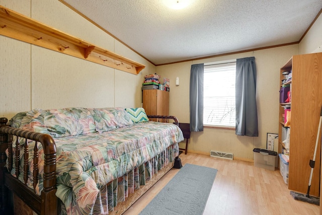 bedroom with vaulted ceiling, wood finished floors, visible vents, and crown molding