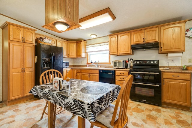 kitchen with a toaster, stone finish flooring, under cabinet range hood, a sink, and black appliances