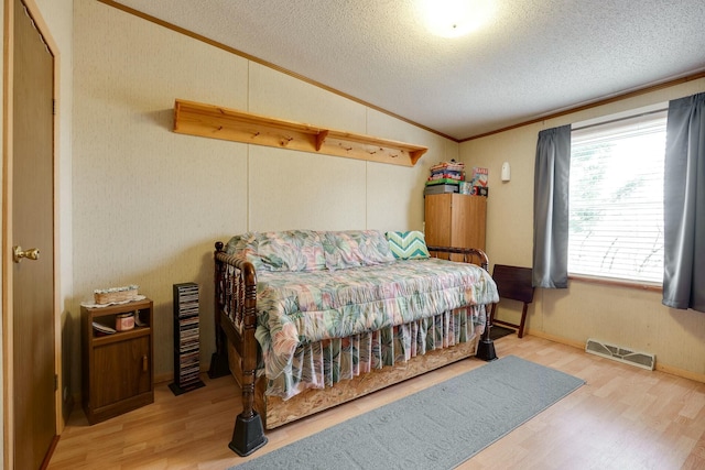 bedroom featuring lofted ceiling, visible vents, ornamental molding, a textured ceiling, and wood finished floors