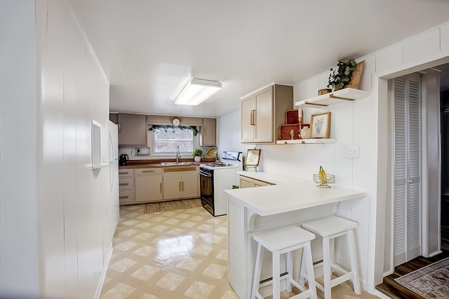 kitchen featuring sink, a kitchen breakfast bar, cream cabinets, white gas range, and kitchen peninsula