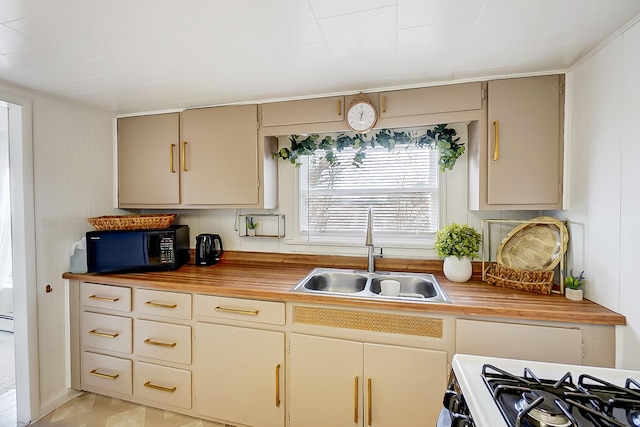 kitchen with butcher block countertops, sink, cream cabinetry, and white gas range