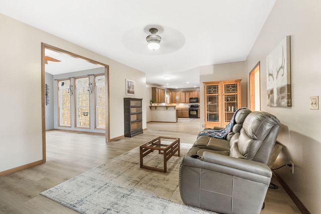 living room featuring a ceiling fan, baseboards, and light wood finished floors