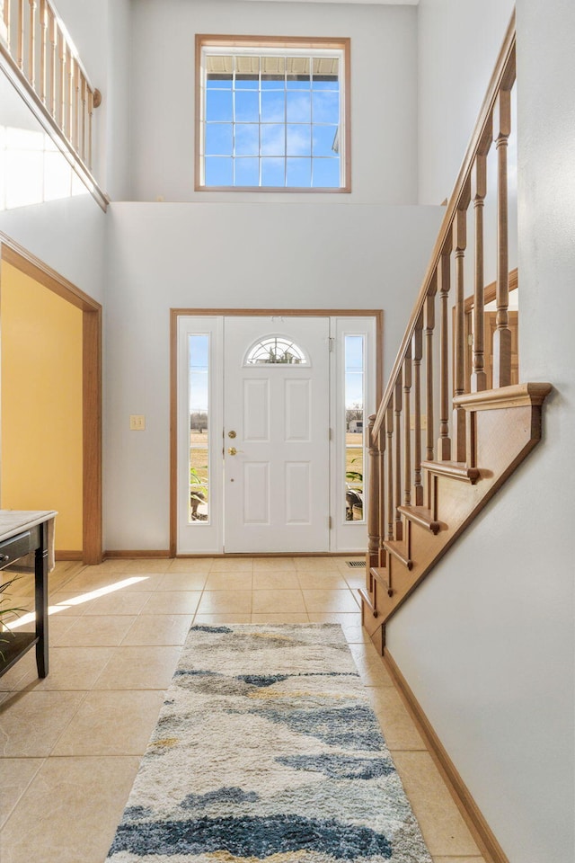 tiled entrance foyer with stairway, baseboards, and a towering ceiling