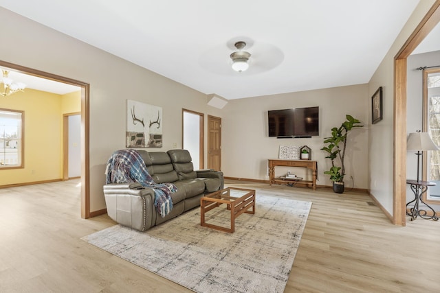 living room featuring ceiling fan with notable chandelier, baseboards, and light wood finished floors