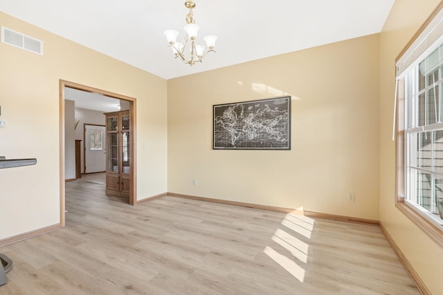 empty room with a notable chandelier, light wood-style floors, visible vents, and baseboards