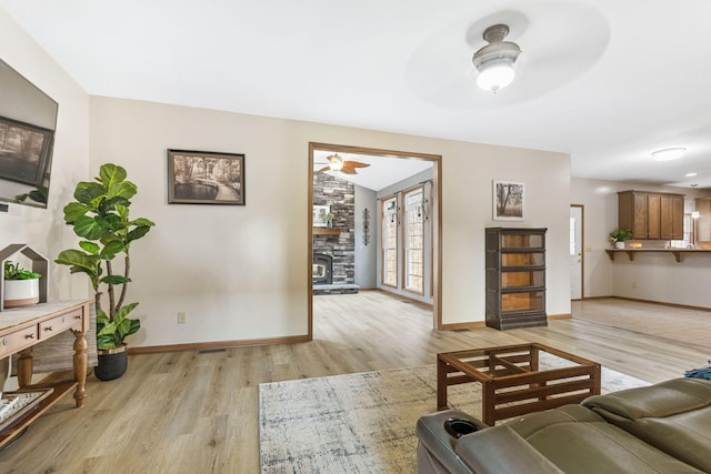 living area with baseboards, ceiling fan, and light wood finished floors