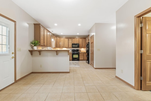 kitchen featuring a breakfast bar, a peninsula, black appliances, and baseboards