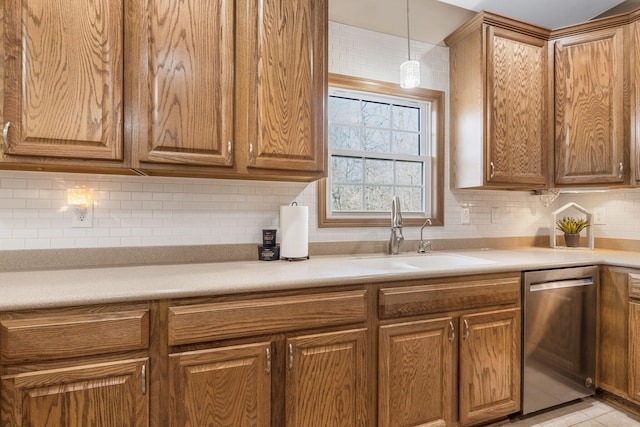 kitchen featuring tasteful backsplash, pendant lighting, light countertops, stainless steel dishwasher, and a sink