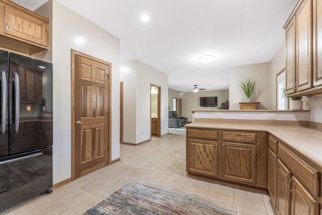 kitchen featuring a ceiling fan, a peninsula, light tile patterned flooring, freestanding refrigerator, and light countertops