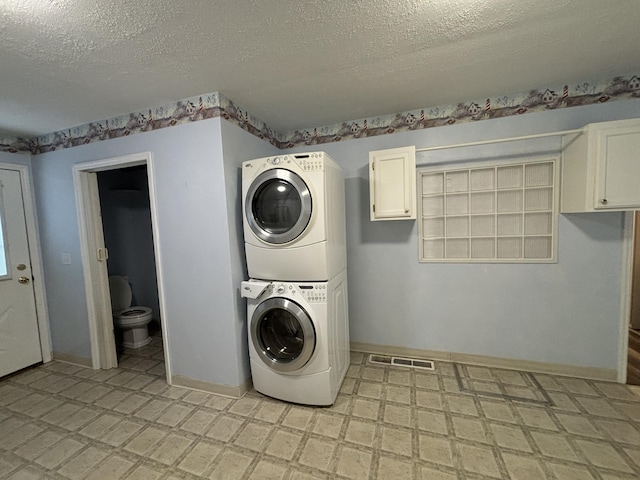 laundry room with stacked washer and clothes dryer, baseboards, a textured ceiling, and light floors