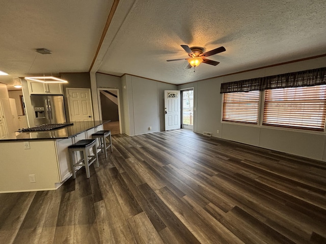 unfurnished living room featuring a ceiling fan, a textured ceiling, visible vents, and dark wood-style flooring