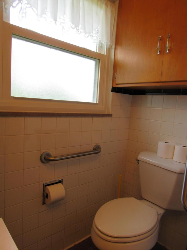 half bath with toilet, plenty of natural light, and tile walls