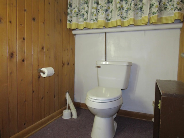 bathroom featuring baseboards, wood walls, and toilet