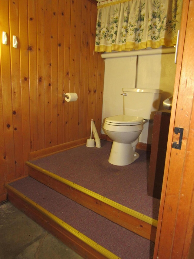 bathroom with toilet, wood walls, and baseboards