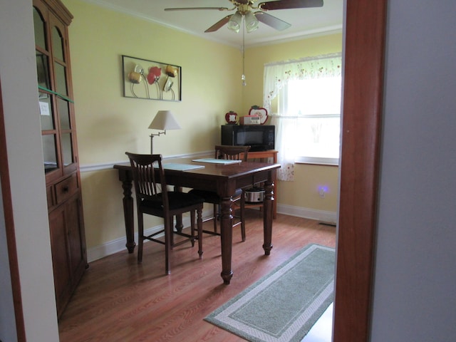dining space with wood finished floors, ceiling fan, crown molding, a desk, and baseboards