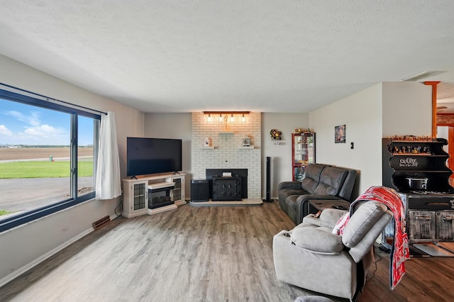 living room with a textured ceiling, visible vents, a brick fireplace, wood finished floors, and baseboards