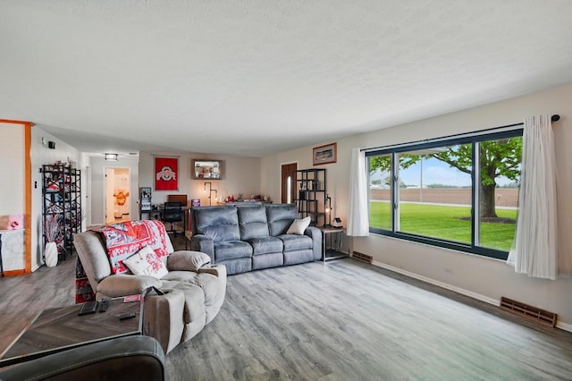 living area with baseboards, a textured ceiling, wood finished floors, and visible vents