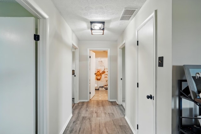 hallway featuring visible vents, a textured ceiling, baseboards, and light wood-style floors
