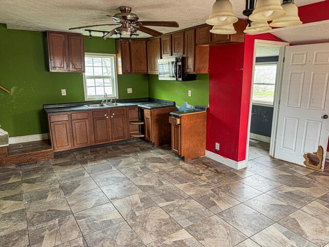 kitchen with baseboards, ceiling fan, stainless steel microwave, dark countertops, and a sink