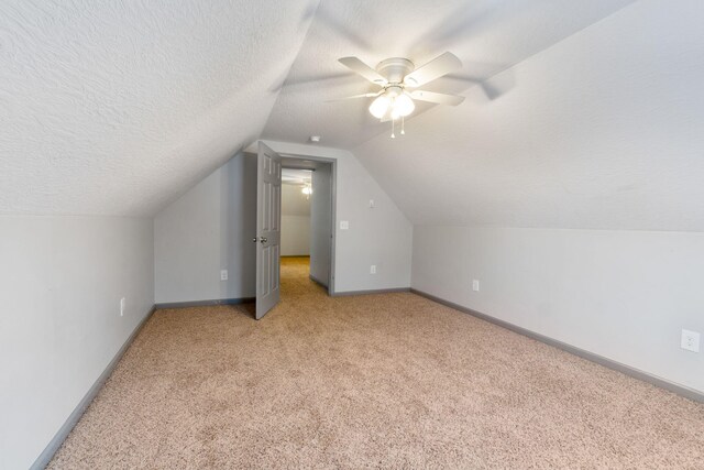 bonus room with a ceiling fan, baseboards, vaulted ceiling, a textured ceiling, and light colored carpet