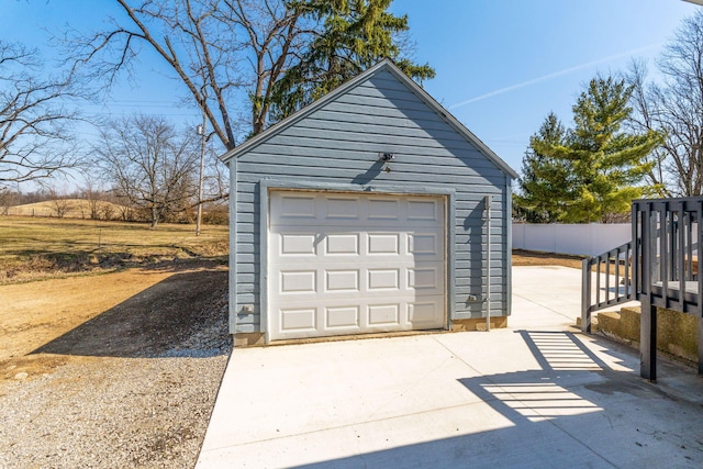 detached garage featuring concrete driveway and fence