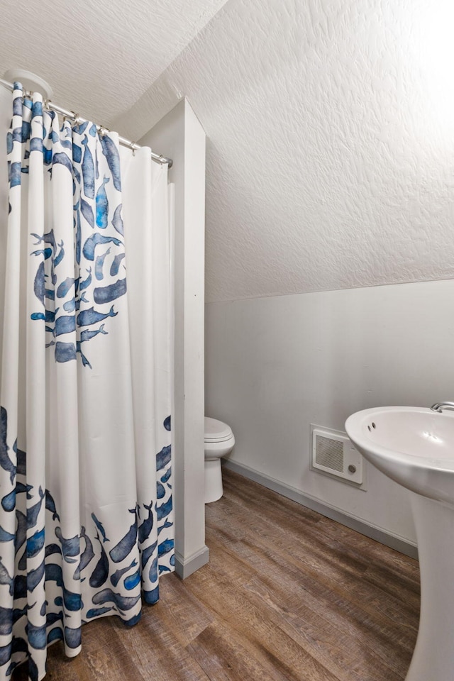 full bathroom featuring baseboards, toilet, vaulted ceiling, wood finished floors, and a textured ceiling