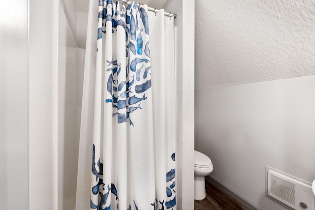 bathroom featuring visible vents, toilet, a textured ceiling, wood finished floors, and vaulted ceiling