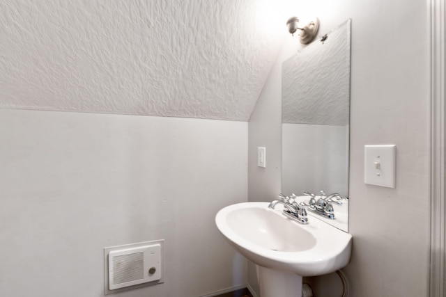 bathroom featuring a sink, lofted ceiling, and a textured ceiling