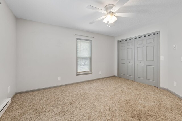 unfurnished bedroom with baseboards, carpet floors, baseboard heating, a closet, and a ceiling fan