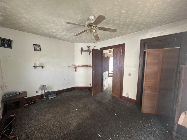 empty room featuring a textured ceiling, dark carpet, and ceiling fan