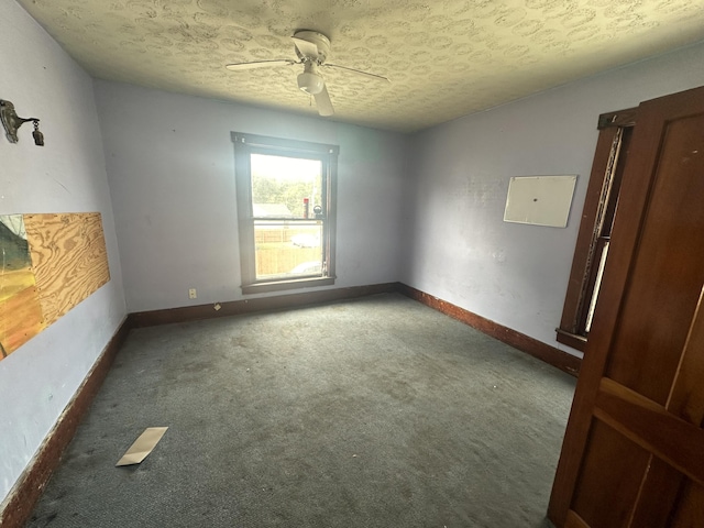 spare room with a textured ceiling, dark colored carpet, and ceiling fan