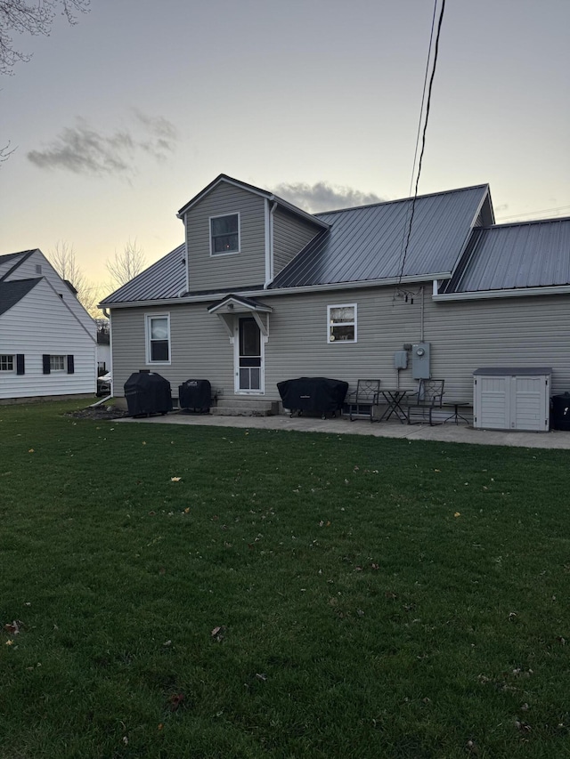 back house at dusk with a lawn and a patio