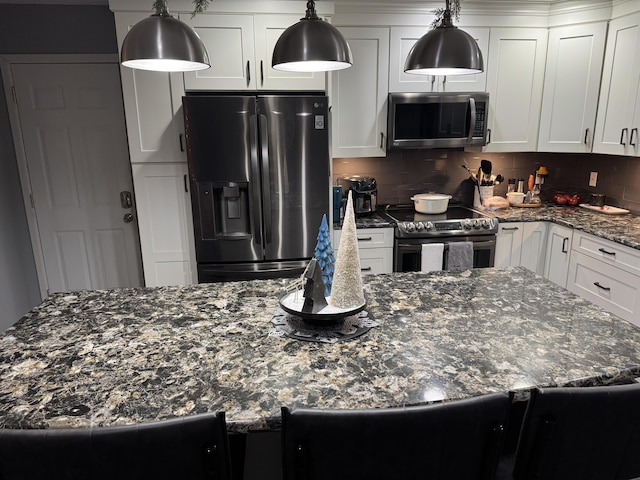 kitchen with appliances with stainless steel finishes, white cabinets, decorative backsplash, decorative light fixtures, and dark stone counters