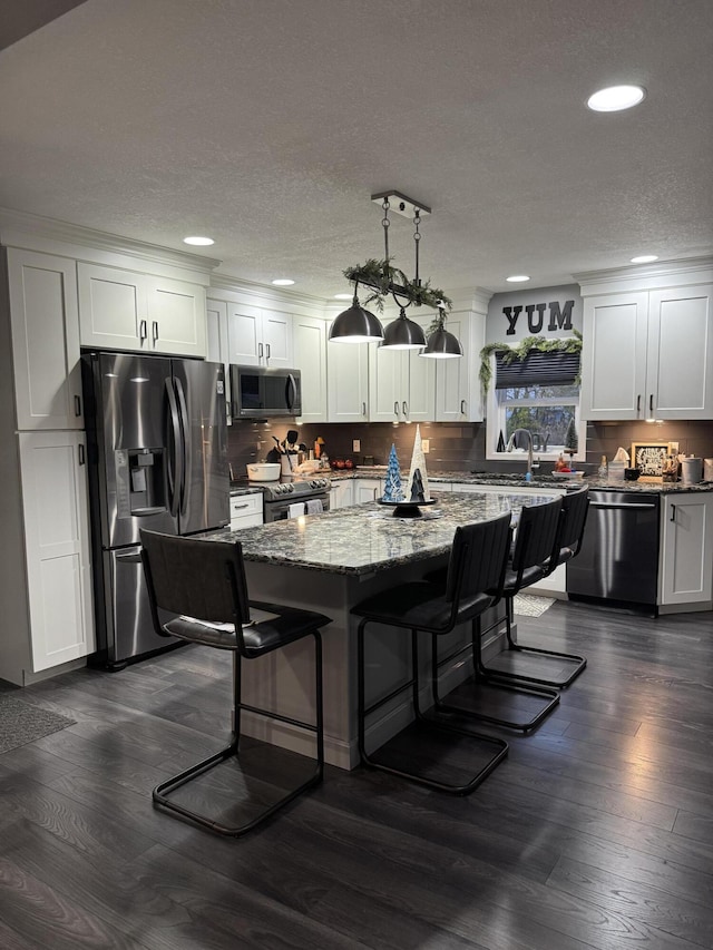 kitchen with a breakfast bar area, dark stone countertops, stainless steel appliances, a center island, and white cabinets