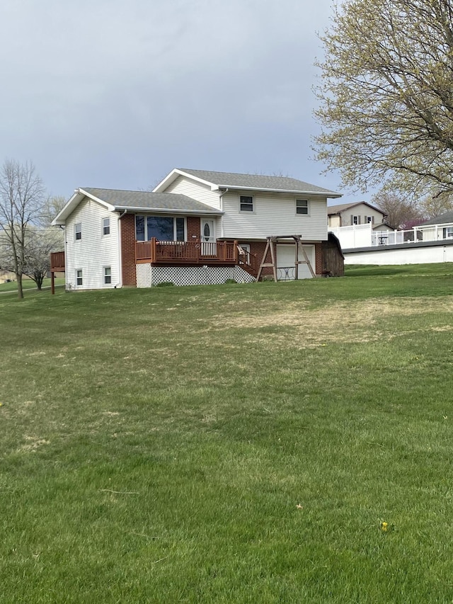 rear view of property featuring an attached garage, a wooden deck, a lawn, and brick siding