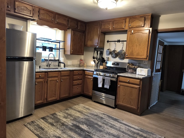 kitchen with stainless steel appliances, light stone countertops, sink, and wood-type flooring