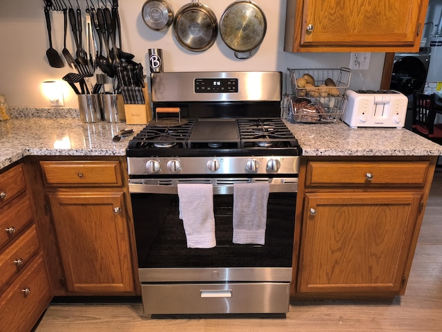 kitchen featuring gas stove, light wood finished floors, brown cabinets, and light stone countertops