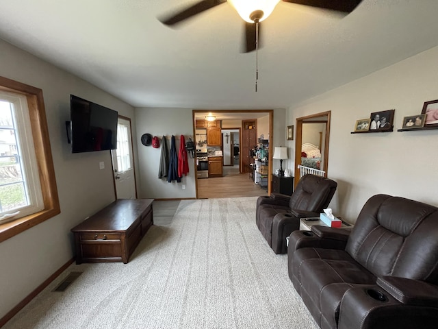 living room featuring ceiling fan, light colored carpet, and baseboards