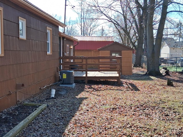 view of yard featuring central AC unit, a wooden deck, a storage shed, fence, and an outdoor structure