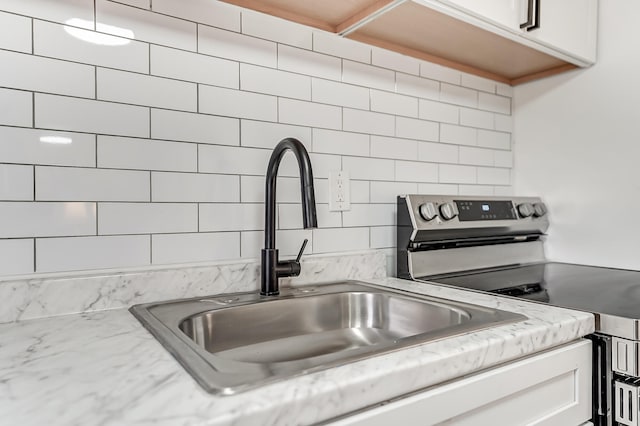 interior details featuring sink, electric range, light stone countertops, white cabinets, and decorative backsplash