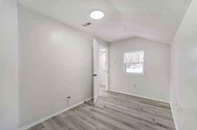 spare room featuring lofted ceiling and light hardwood / wood-style floors