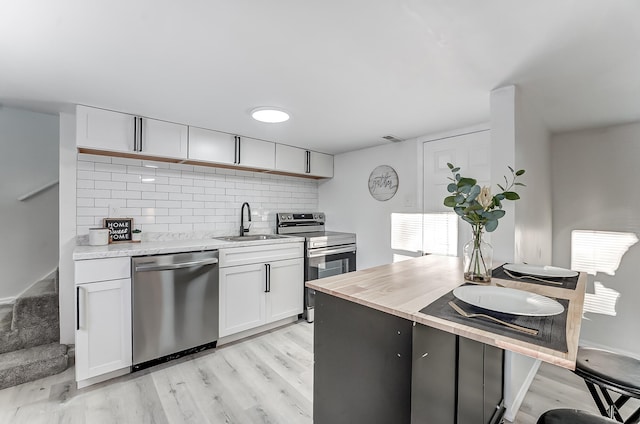 kitchen featuring sink, white cabinetry, light wood-type flooring, stainless steel appliances, and decorative backsplash