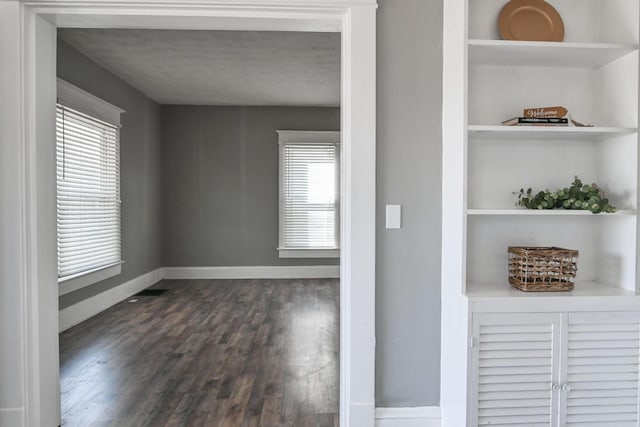 empty room with plenty of natural light, built in shelves, baseboards, and dark wood-style flooring