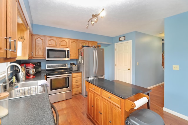 kitchen with light wood-style flooring, dark countertops, a sink, stainless steel appliances, and a breakfast bar area