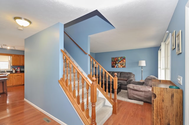 stairs with rail lighting, visible vents, baseboards, and wood finished floors