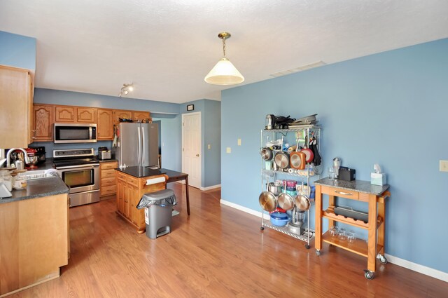 kitchen with baseboards, a sink, dark countertops, light wood-style floors, and stainless steel appliances